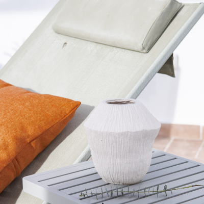 Vaso branco de cerâmica numa mesa cinzenta ao lado de uma espreguiçadeira com almofada laranja