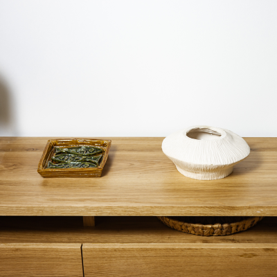 Tabuleiro castanho com peças verdes e vaso branco com textura sobre móvel de madeira