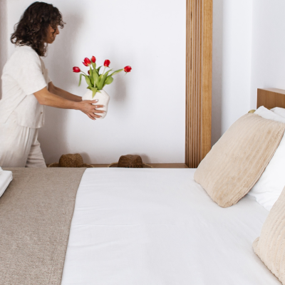 Quarto com cama branca, almofadas bege e vaso com tulipas vermelhas