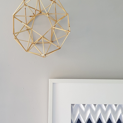 Suspensão decorativa geométrica suspendida numa parede cinza com moldura branca e imagem abstrata azul e cinzenta