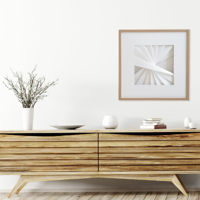 Aparador de madeira clara com decorações e quadro geométrico branco na parede