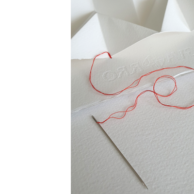 Agulha de costura com linha vermelha sobre papel e papel branco com palavra em relevo