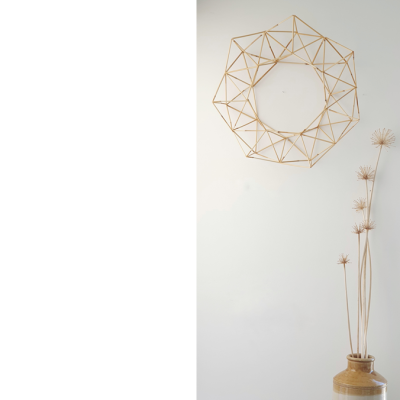 Decoração de parede com objeto geométrico em madeira clara e vaso de cerâmica com plantas secas
