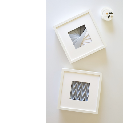 Dois quadros abstratos em branco e cinza em superfície branca com vela decorativa branca