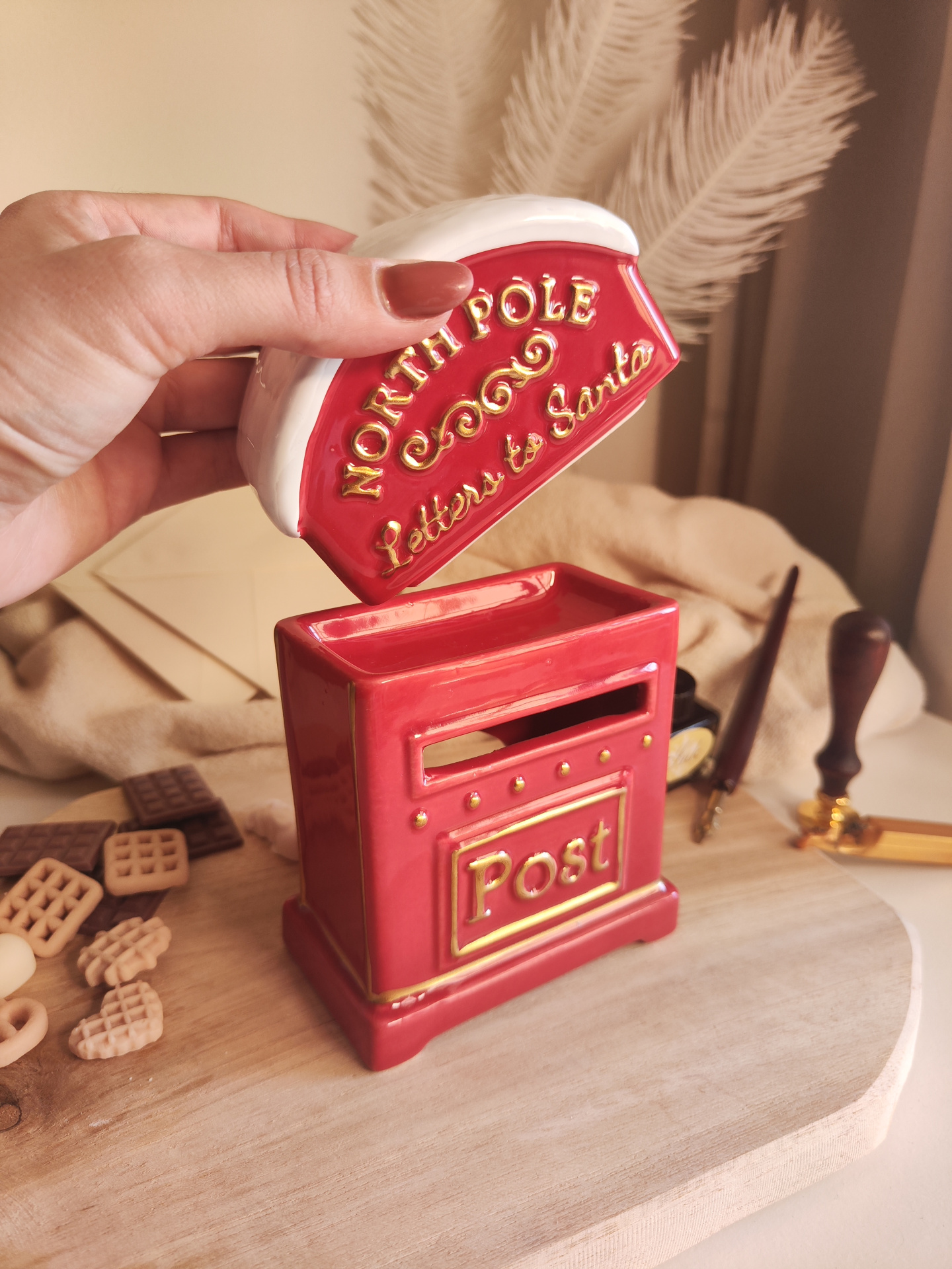 Queimador Cartas ao Pai Natal Caixa vermelha em cerâmica com tampa branca e letras douradas, decorada e segurada por uma mão.
