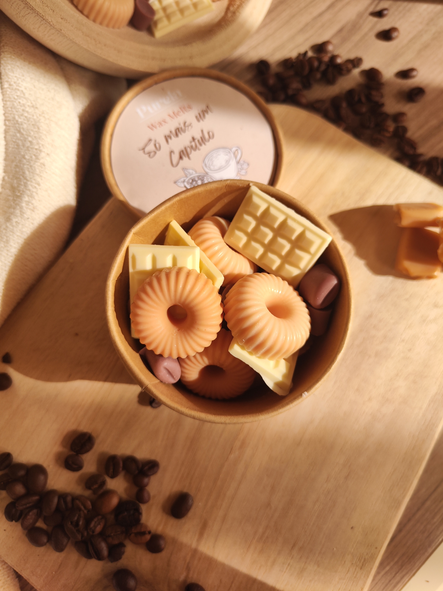 Wax Melt Só mais um Capítulo Vaso redondo com velas multiformas cor creme e alaranjado sobre tábua de madeira com grãos de café