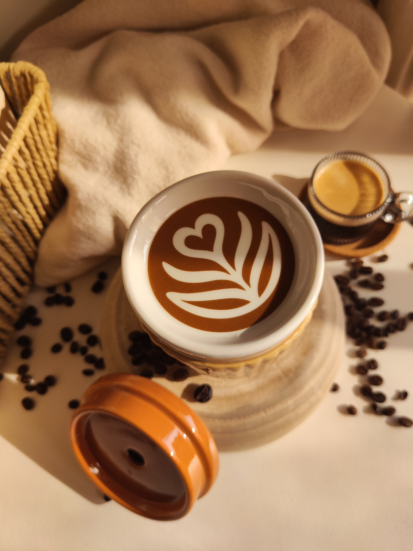 Queimador Copo de café Caneca com latte art em forma de coração e folhas ao lado de tampa castanha e chávena de espresso com grãos de café