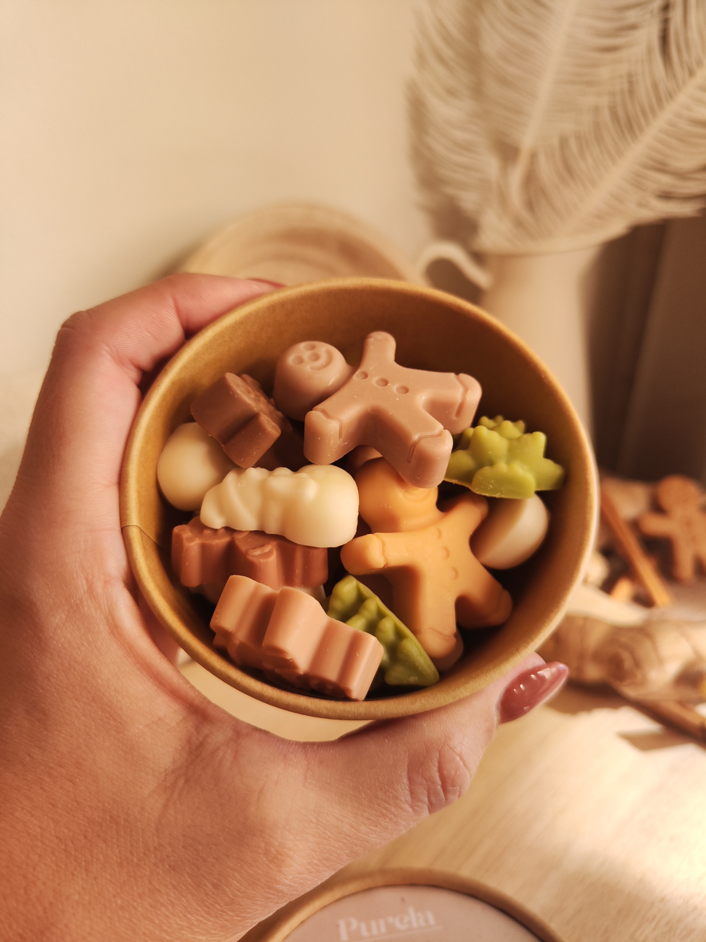 Wax Melt Conto de Gengibre Taça castanha com sabonetes em forma de figuras natalícias coloridas, mão segurando taça.