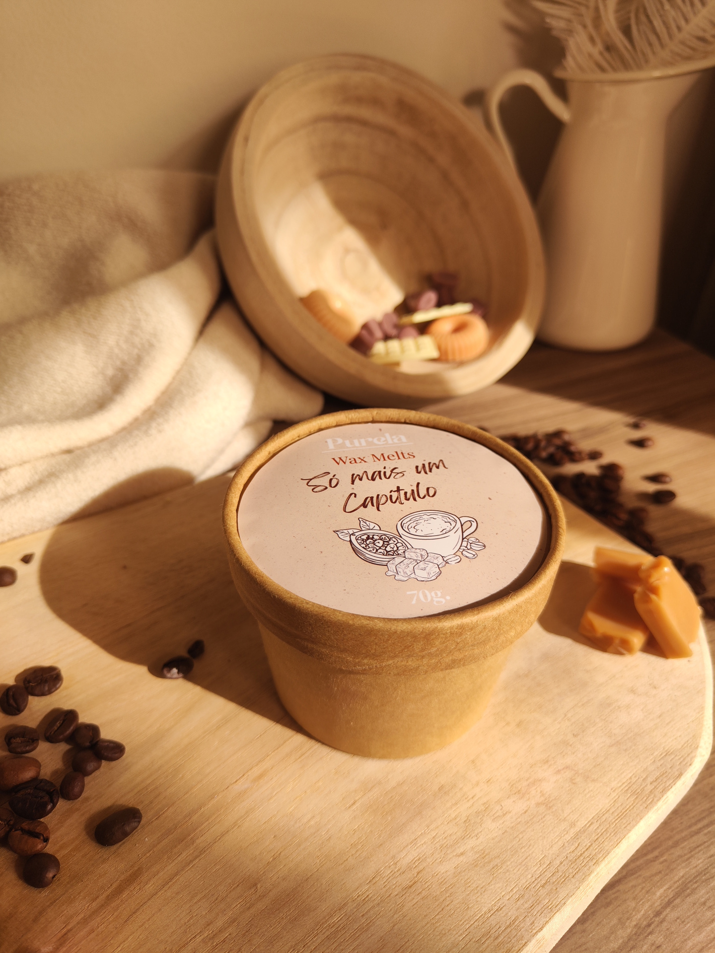Wax Melt Só mais um Capítulo Embalagem de Wax Melts com texto Só mais um Capítulo e grãos de café numa tábua de madeira