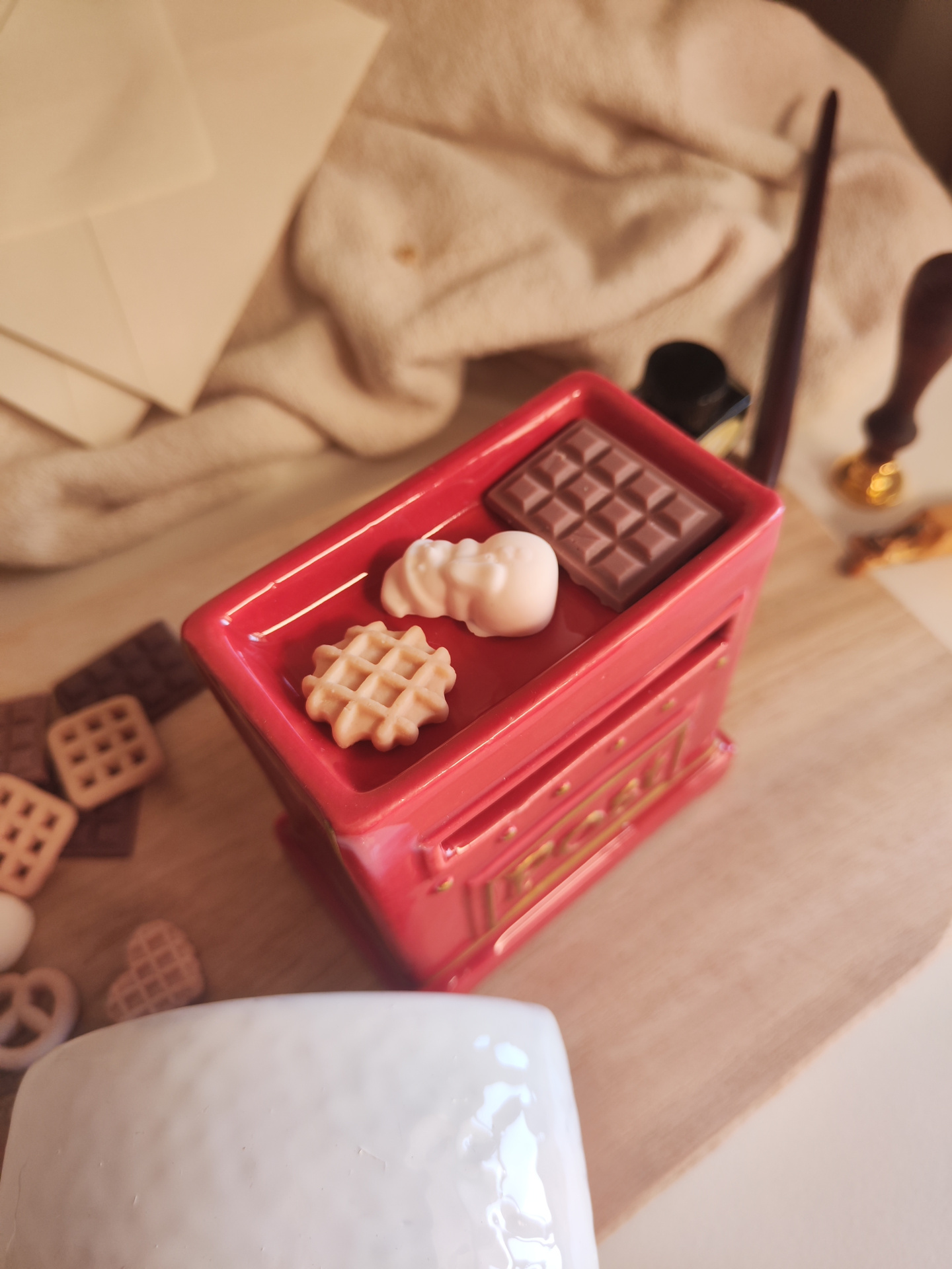 Queimador Cartas ao Pai Natal Miniaturas de bolachas e chocolate sobre superfície vermelha esmaltada com relevo.