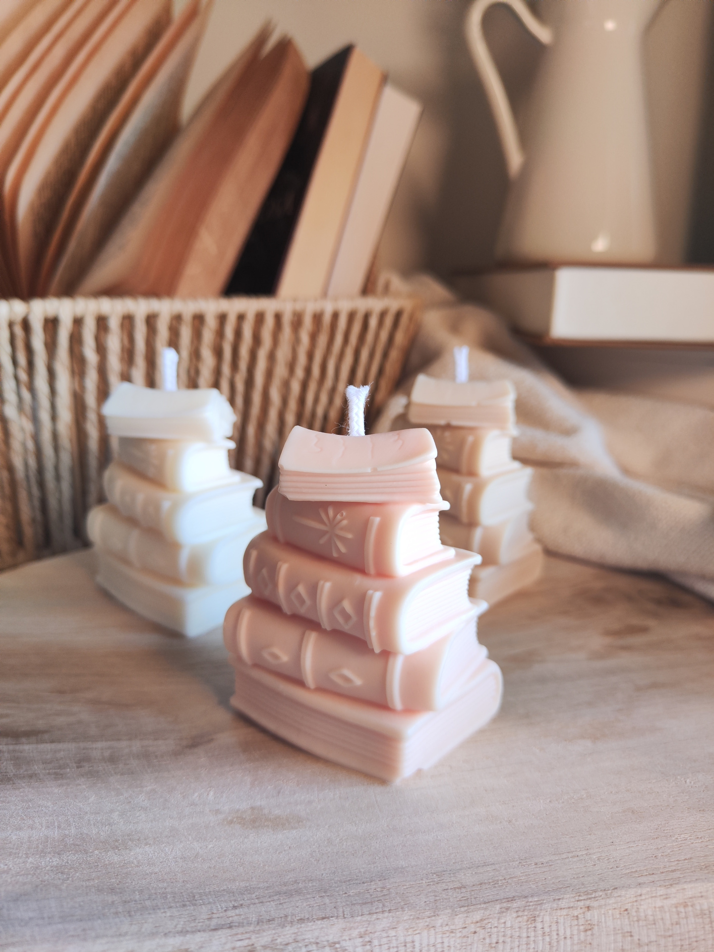 Vela TBR Velas decorativas em forma de pilhas de livros sobre superfície de madeira com cesta de vime e jarro branco ao fundo