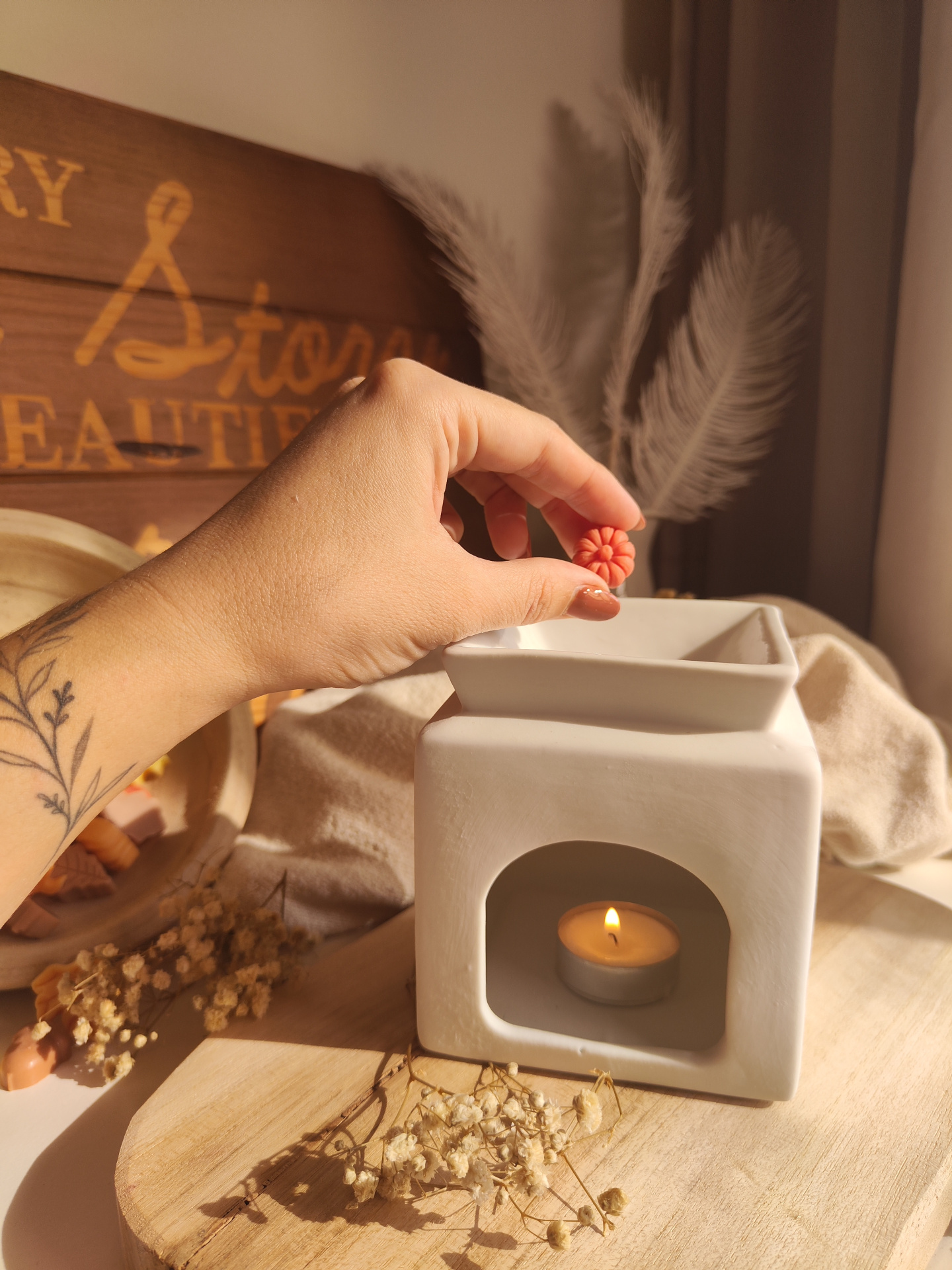 Queimador Casa Difusor cerâmico branco com vela, mão segurando pastilha perfumada laranja em forma de flor