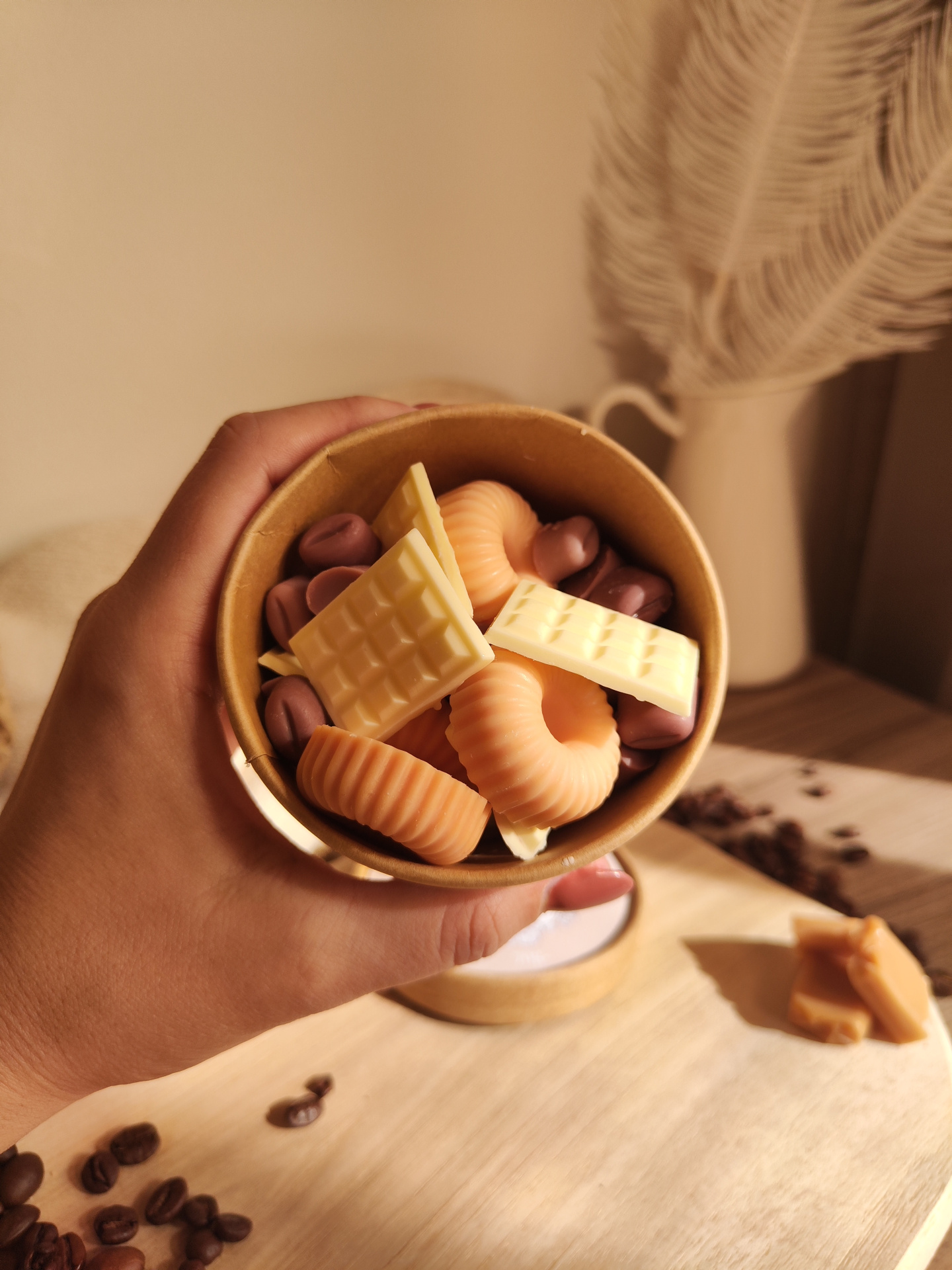 Wax Melt Só mais um Capítulo Recipiente de cartão com sabonetes coloridos segurado por mão sobre superfície de madeira com grãos de café.