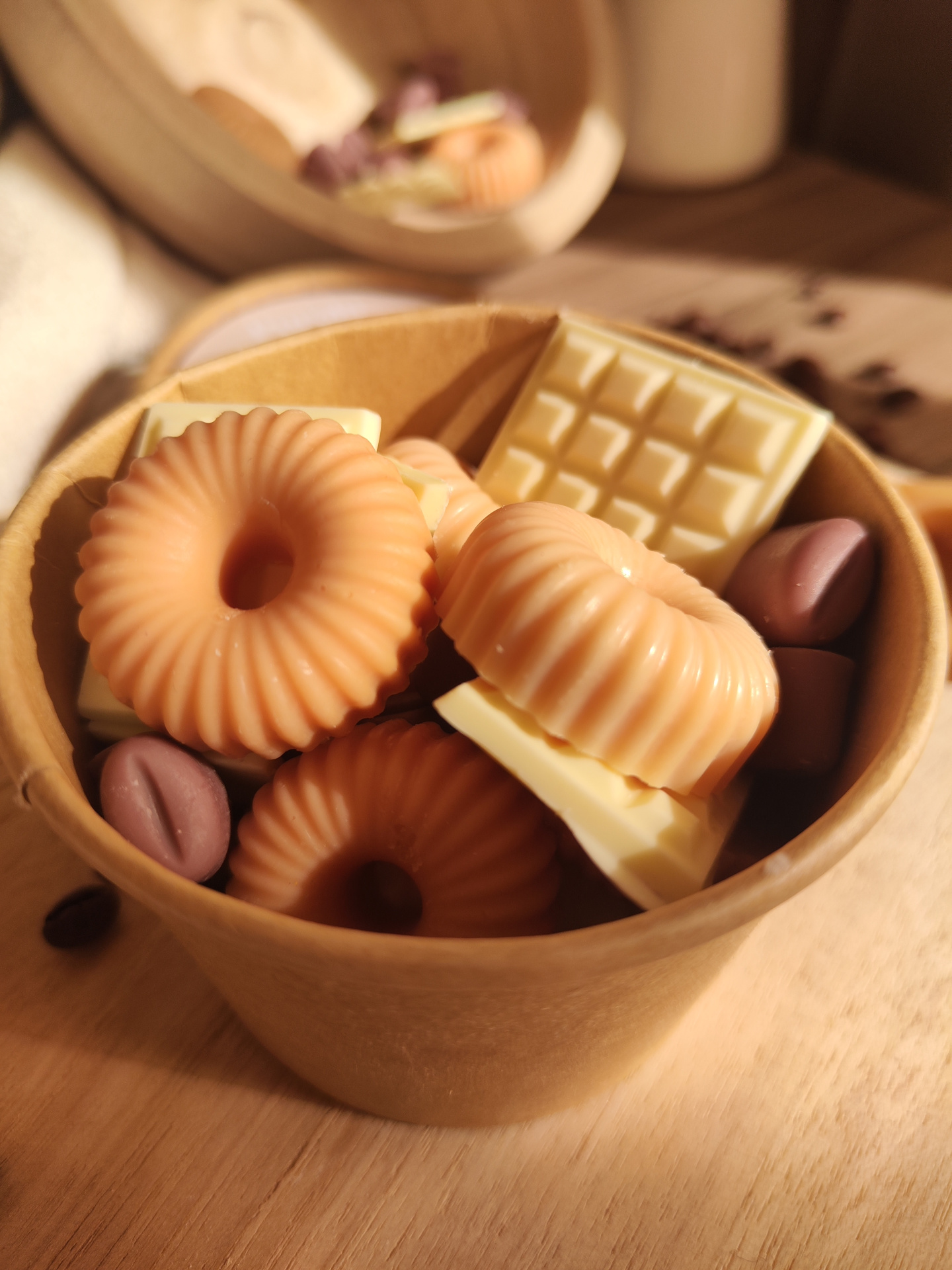 Wax Melt Só mais um Capítulo Caixa redonda com sabonetes de formas variadas, incluindo tabletes de chocolate branco, anéis cor de pêssego e grãos de café castanhos.