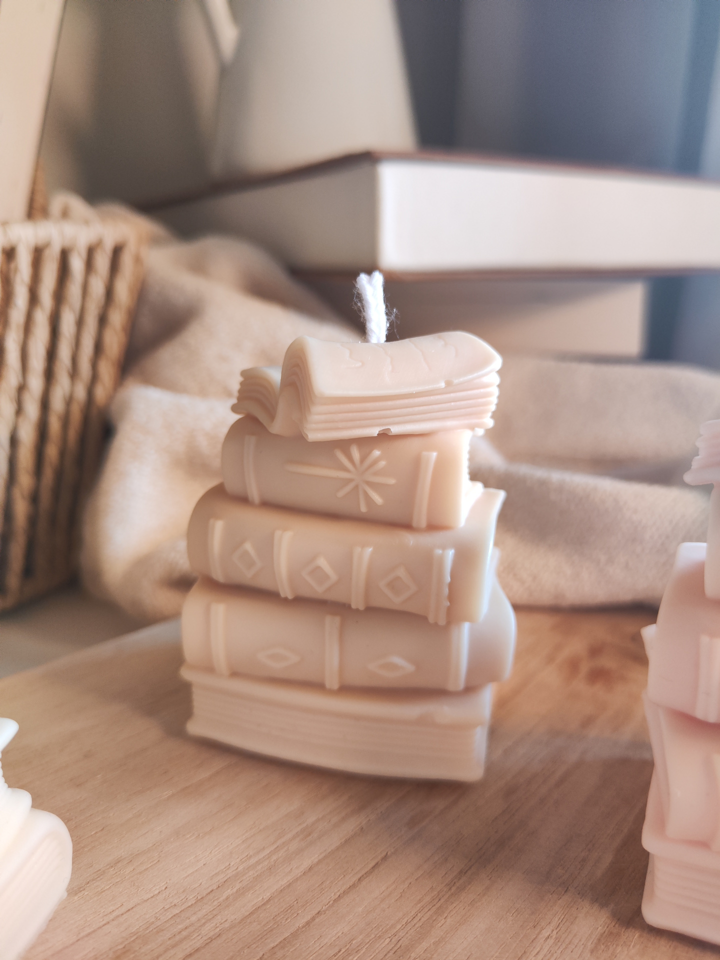 Vela TBR Vela em forma de pilha de livros creme sobre mesa de madeira com tecido bege ao fundo