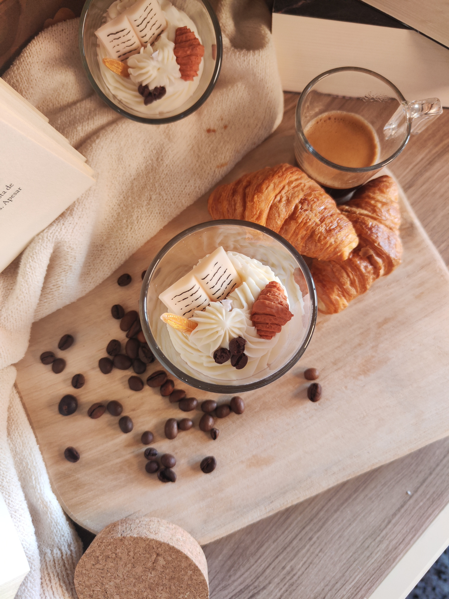 Vela Só mais um Capítulo Sobremesas em copos de vidro, croissants, chávena de café, grãos de café e livro sobre tábua de madeira e tecido bege