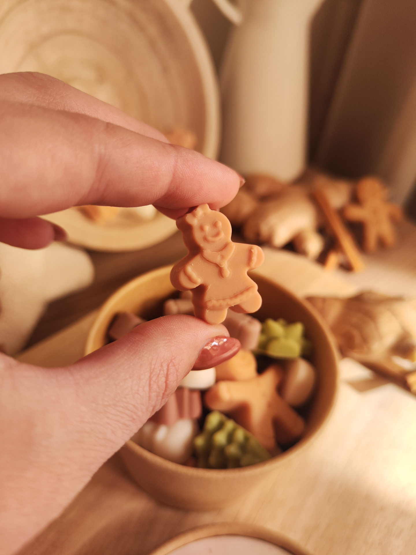 Wax Melt Conto de Gengibre Figura pequena de homem de gengibre laranja segurada pela mão, com recipiente de madeira e elementos decorativos ao fundo