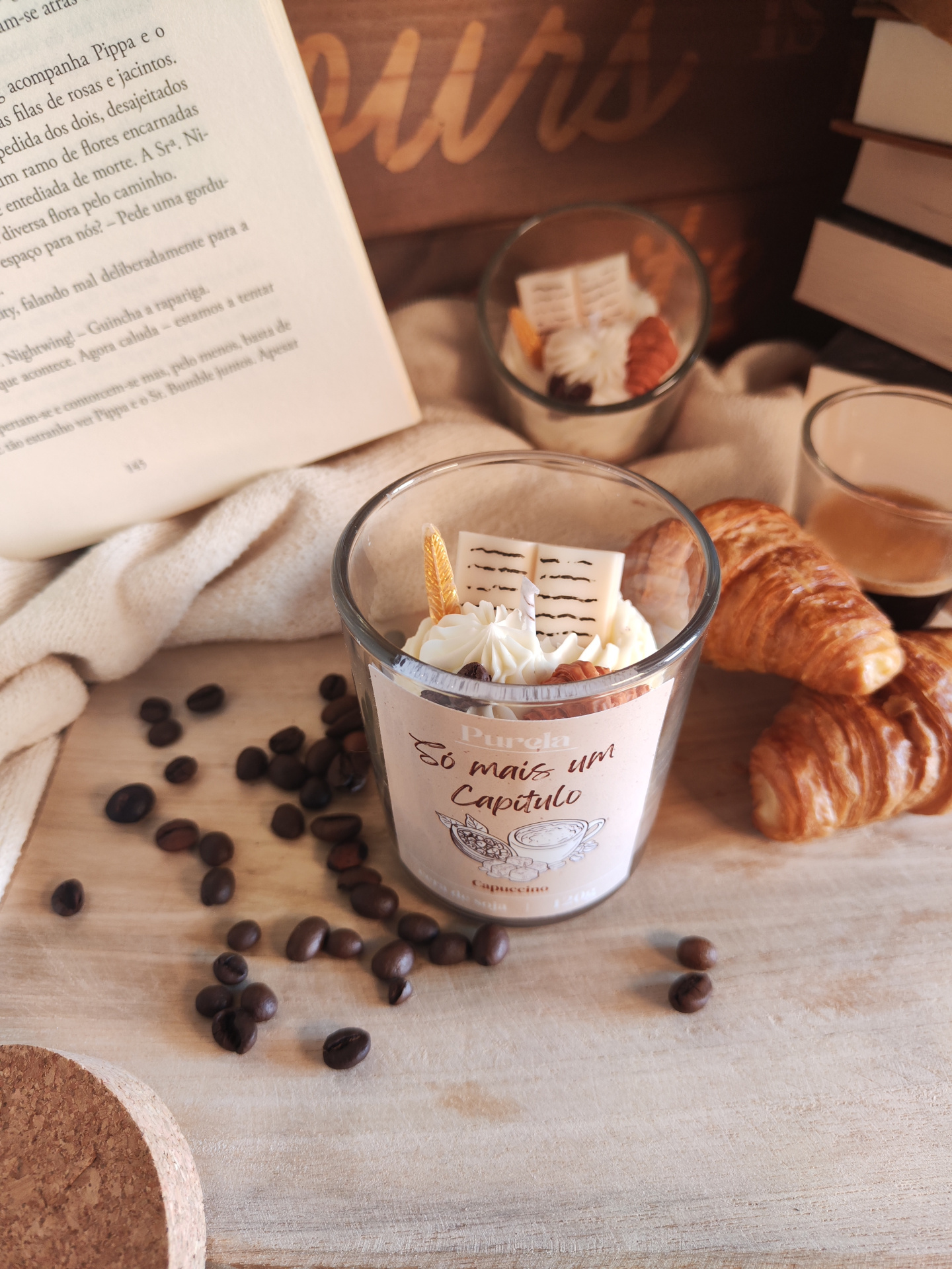 Vela Só mais um Capítulo Vela decorativa em copo com rótulo Purela só mais um capítulo, croissants, grãos de café e livro aberto