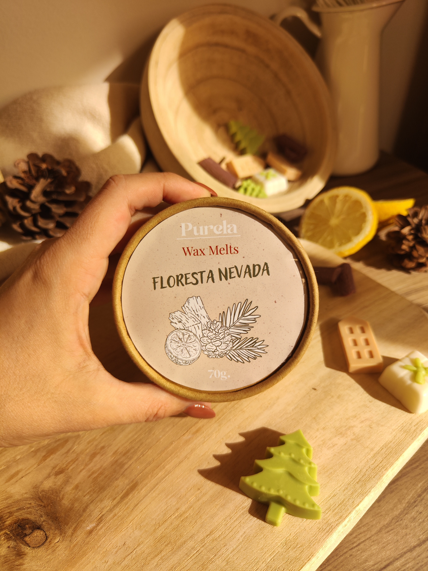 Wax Melt Floresta Nevada Embalaigem redonda de cera aromática Purela com texto FLORESTA NEVADA e peças em forma de árvores e objetos natalícios numa mesa de madeira