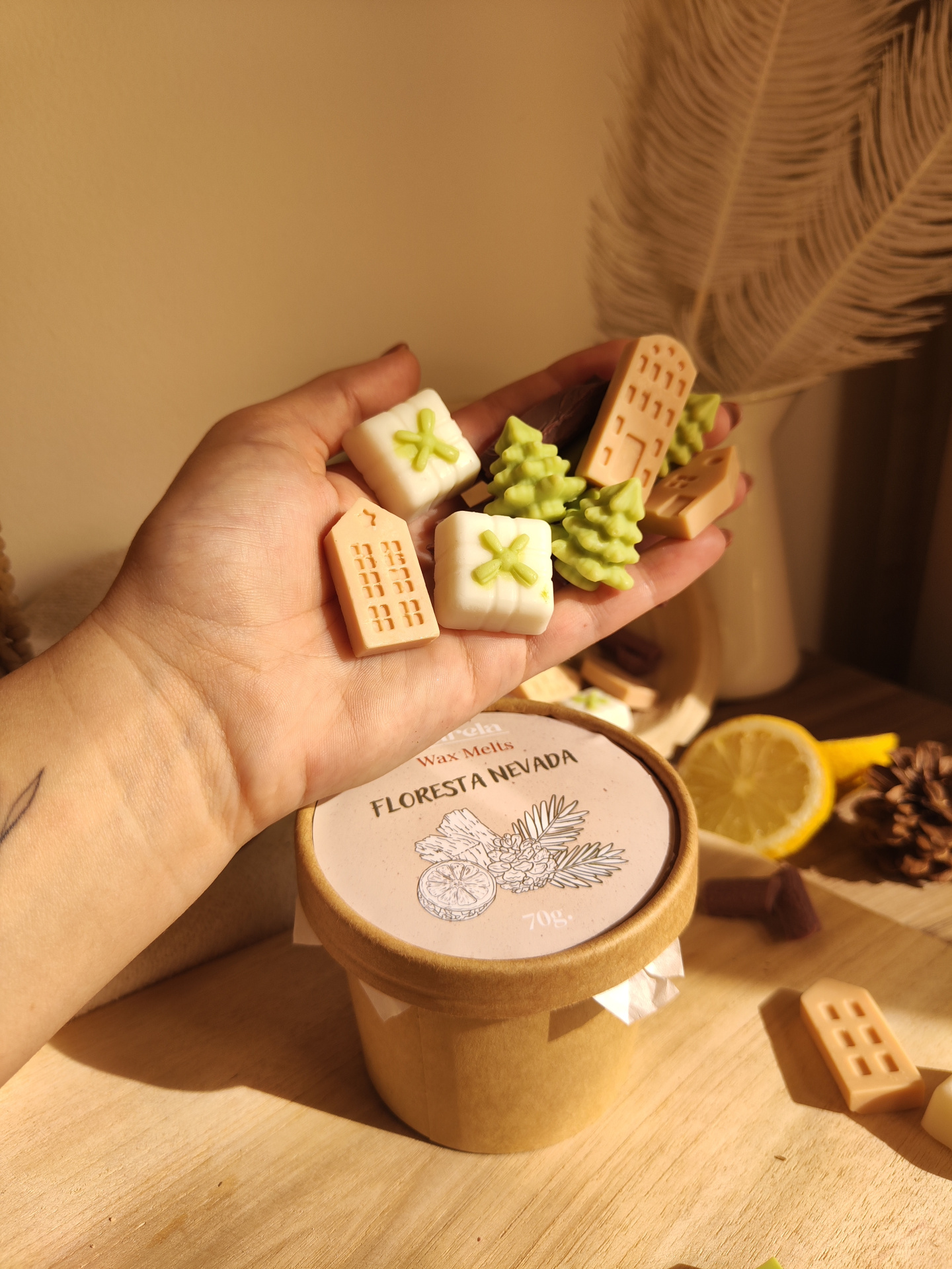Wax Melt Floresta Nevada Objetos decorativos em forma de árvores, casas e presentes, com pote rotulado FLORESTA NEVADA e fatias de limão no fundo
