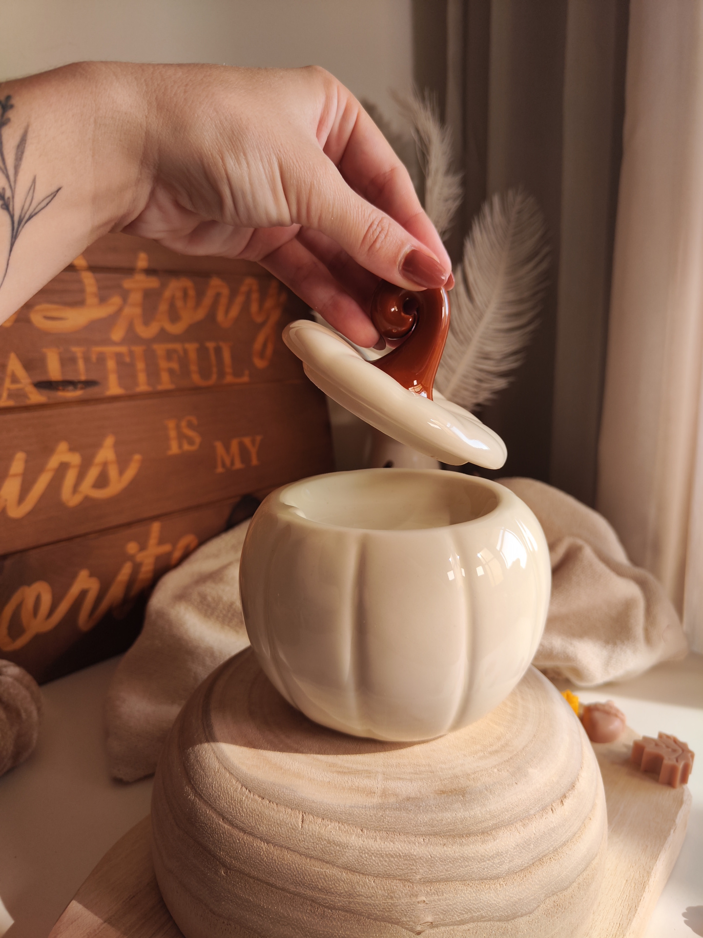 Queimador Abóbora Branca Recipiente de cerâmica creme em forma de abóbora com tampa castanha e base de madeira clara.