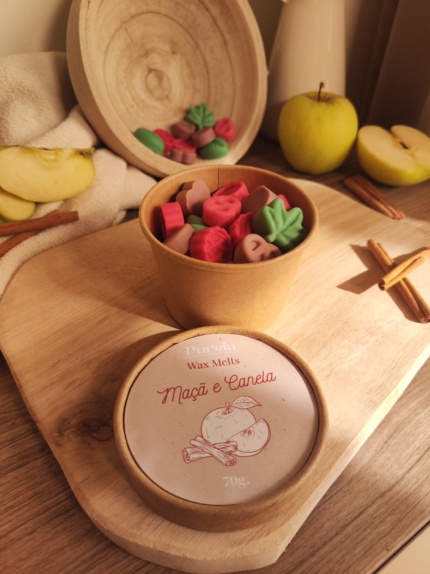 Wax Melt Maçã e Canela Recipiente de cartão com cera em pastilhas coloridas e ingredientes naturais em cima de tábua de madeira