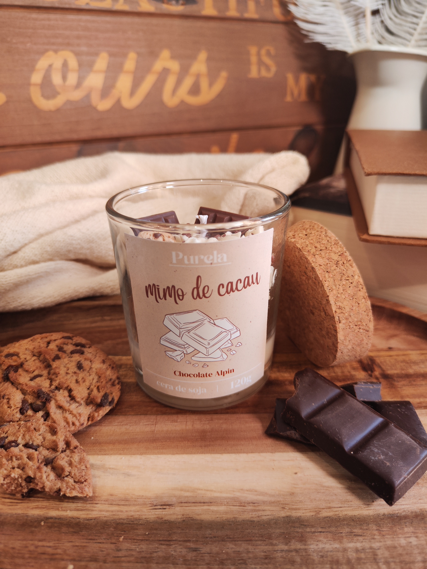 Vela Mimo de Cacau Vela em copo de vidro com rótulo Purela mimo de cacau e pedaços de chocolate ao redor.