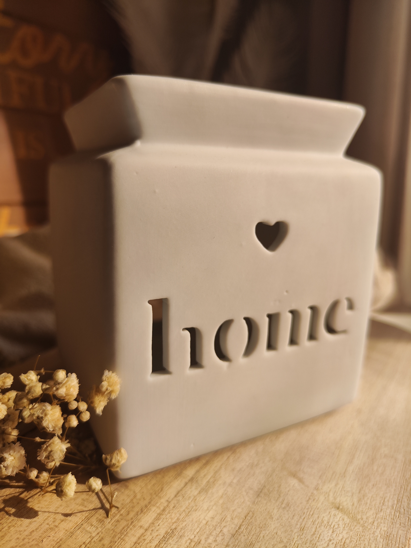Queimador Casa Recipiente decorativo branco com palavra home recortada e um coração, sobre madeira com flores secas.