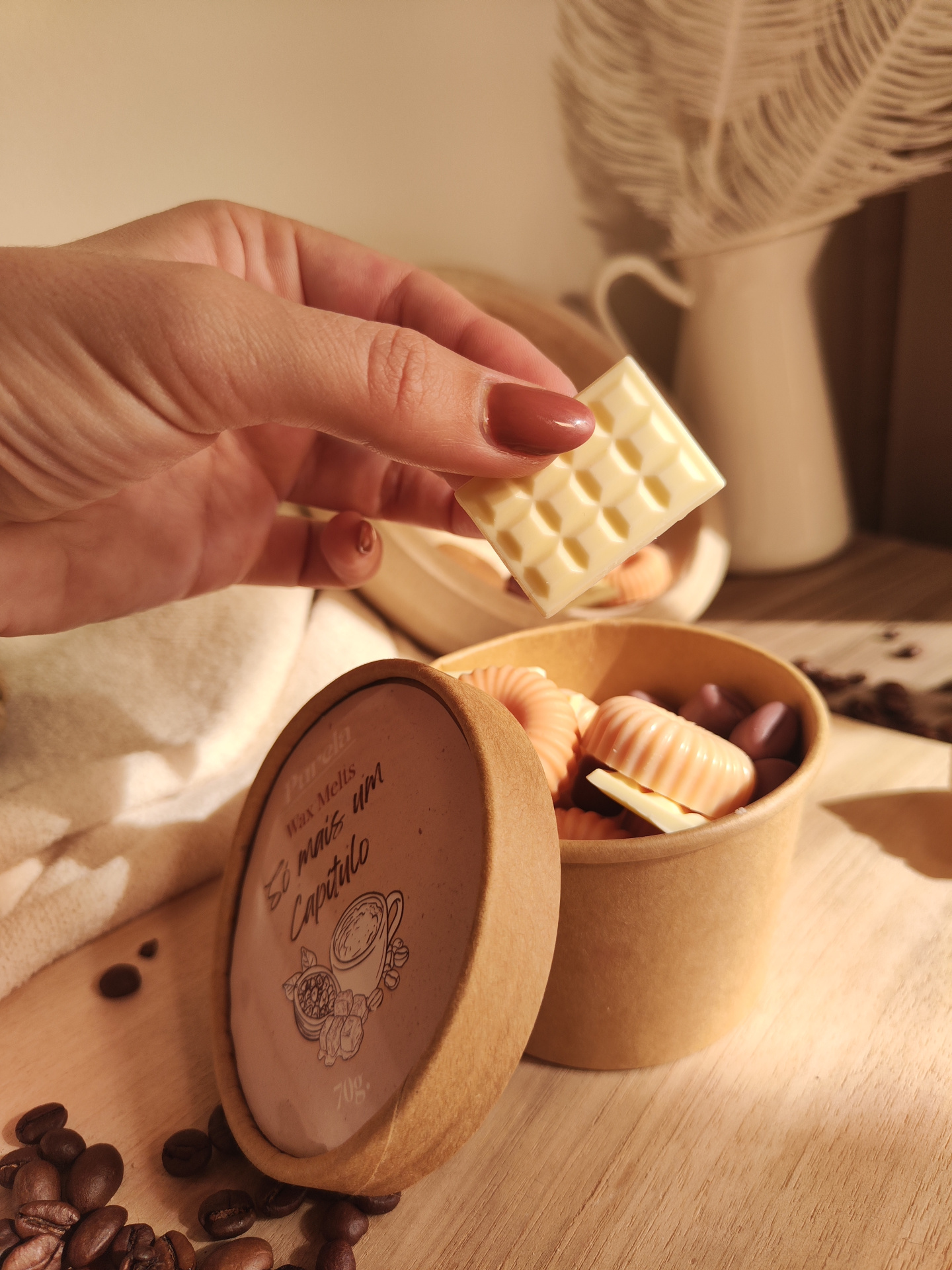 Wax Melt Só mais um Capítulo Mão segurando bloco branco de cera com caixa redonda e feijões de café sobre mesa de madeira