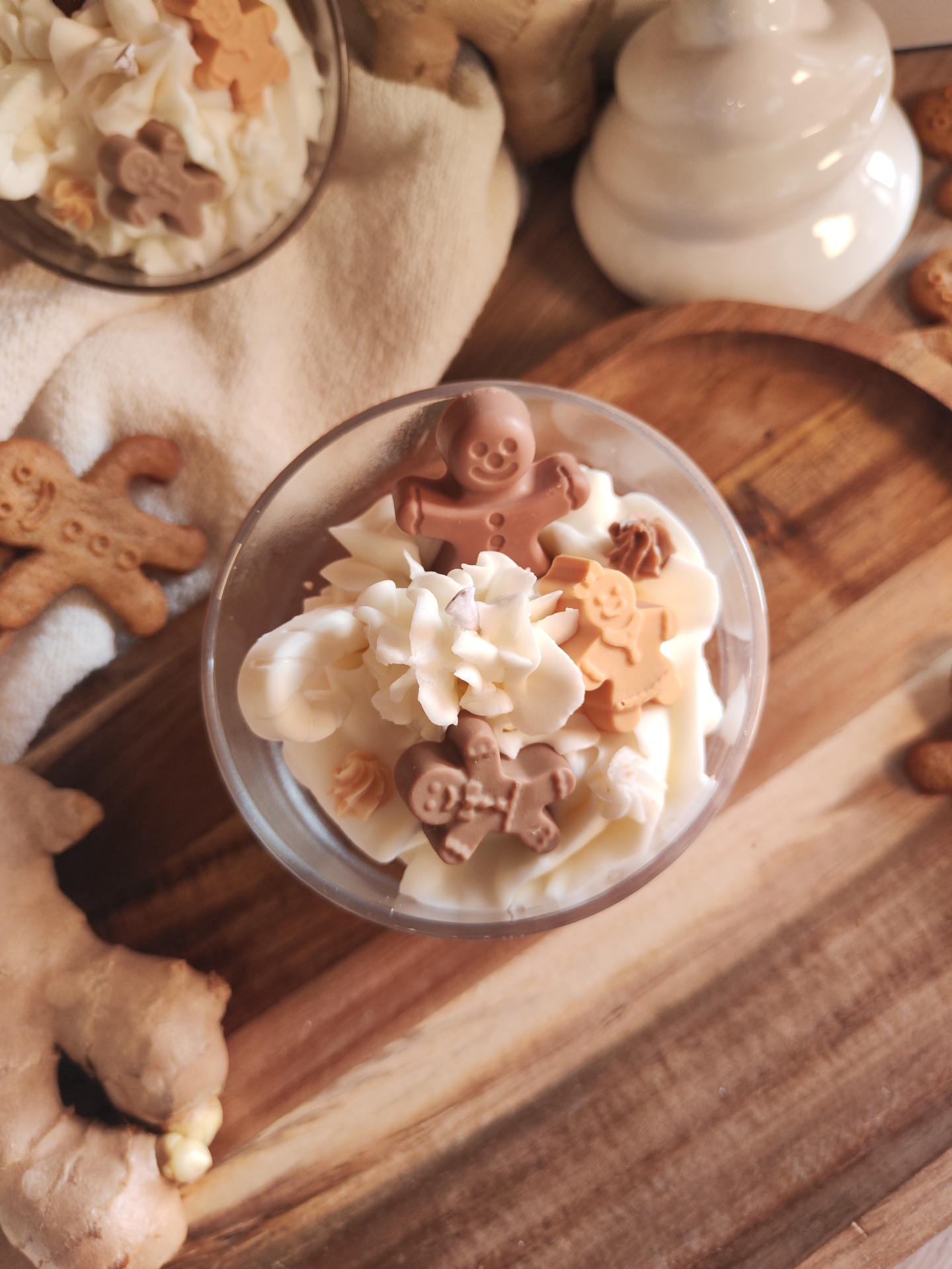 Vela grande Conto de Gengibre Copos de vidro com chantilly e biscoitos de gengibre em forma de boneco, sobre pano bege e tábua de madeira clara