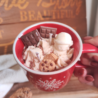 Caneca vermelha com decoração de floco de neve branco, chantilly e chocolates, sobre tábua de madeira com biscoitos