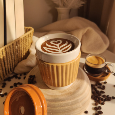 Conjunto de chávena de cerâmica com café decorado ao lado de copo de vidro com expresso e grãos de café