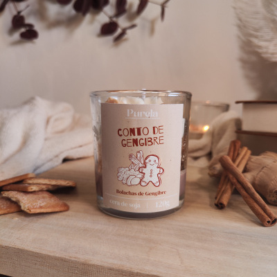 Vela em copo de vidro com rótulo Cono de Gengibre, biscoitos e paus de canela em fundo neutro