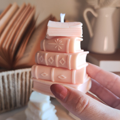 Vela decorativa cor-de-rosa em forma de pilha de livros segurada por mão femininas