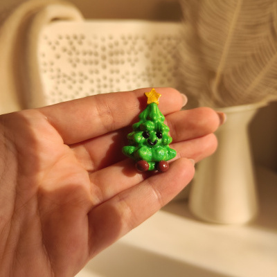 Ornamento pequeno de árvore de Natal verde com rosto sorridente na mão
