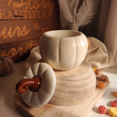 Jarro cerâmico branco com tampa castanha em forma de abóbora sobre base de madeira com decoração de outono.