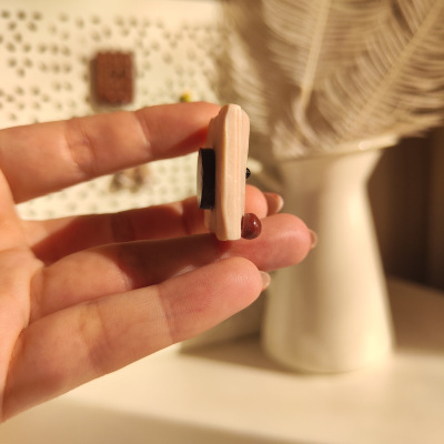 Mão segurando pequeno objeto retangular cor de rosa com bolinhas pretas e castanhas