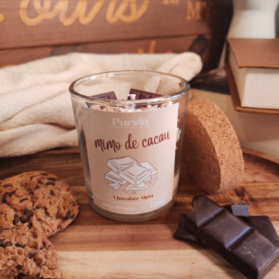 Vela em copo de vidro com rótulo Purela mimo de cacau e pedaços de chocolate ao redor.