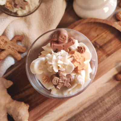 Copos de vidro com chantilly e biscoitos de gengibre em forma de boneco, sobre pano bege e tábua de madeira clara