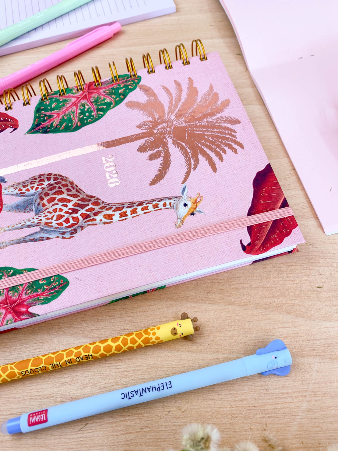Agenda 2023 rosa com estampa de girafa e folhas, lápis amarelo e azul em mesa