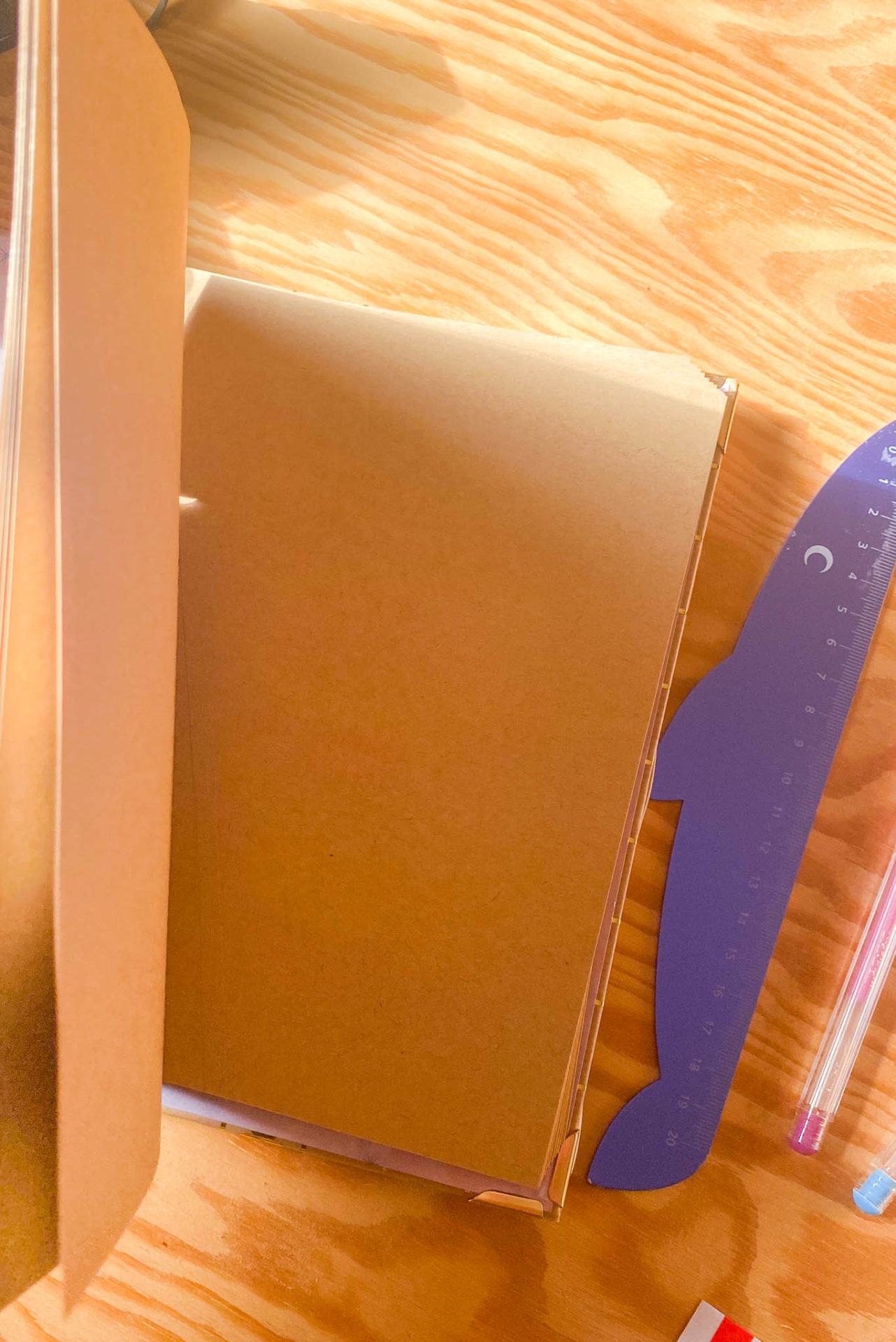 Caderno castanho aberto, régua roxa e caneta roxa sobre mesa de madeira