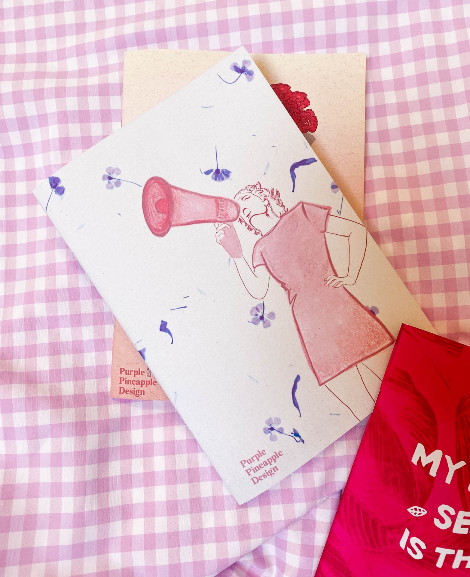 Três cadernos com capas coloridas sobre tecido xadrez rosa e branco