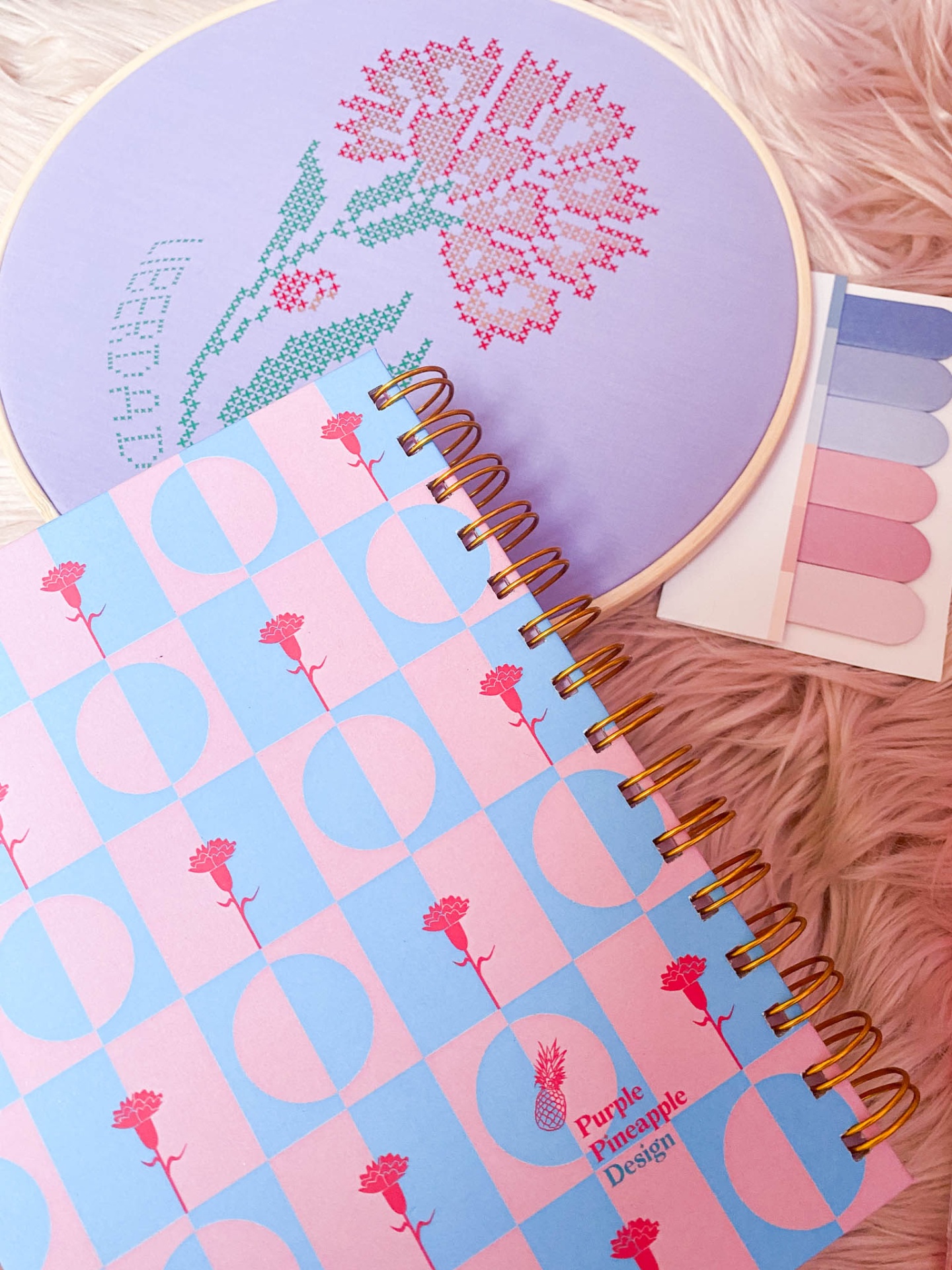 caderno espiral colorido sobre superfície peluda junto a bastidor de bordado e marcador