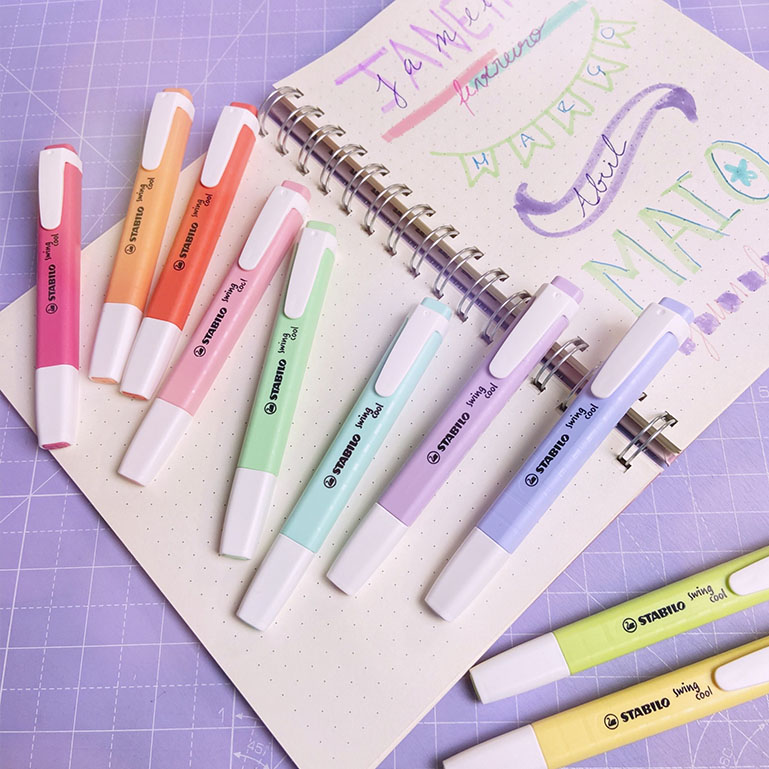Nove marcadores STABILO BOSS cores pastel sobre caderno aberto pontilhado com escritas coloridas