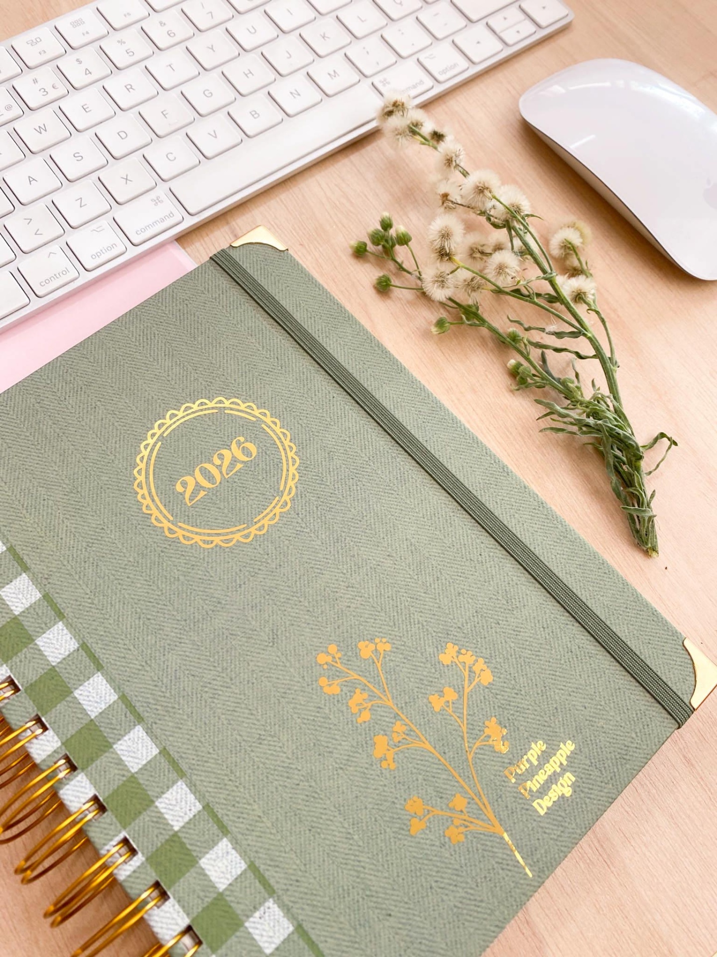 Agenda 2026 verde com flores amarelas e elástico cinza junto a teclado e rato