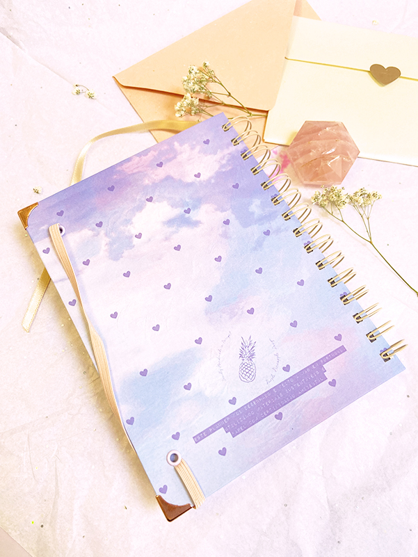 Caderno lilás com corações pequenos e abacaxi, envelopes com selo de coração, flores e cristal rosa