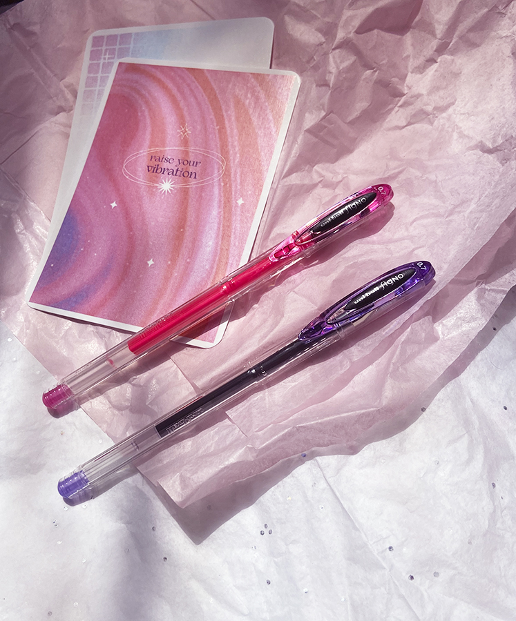 Duas canetas gel e dois cadernos pequenos coloridos sobre papel seda