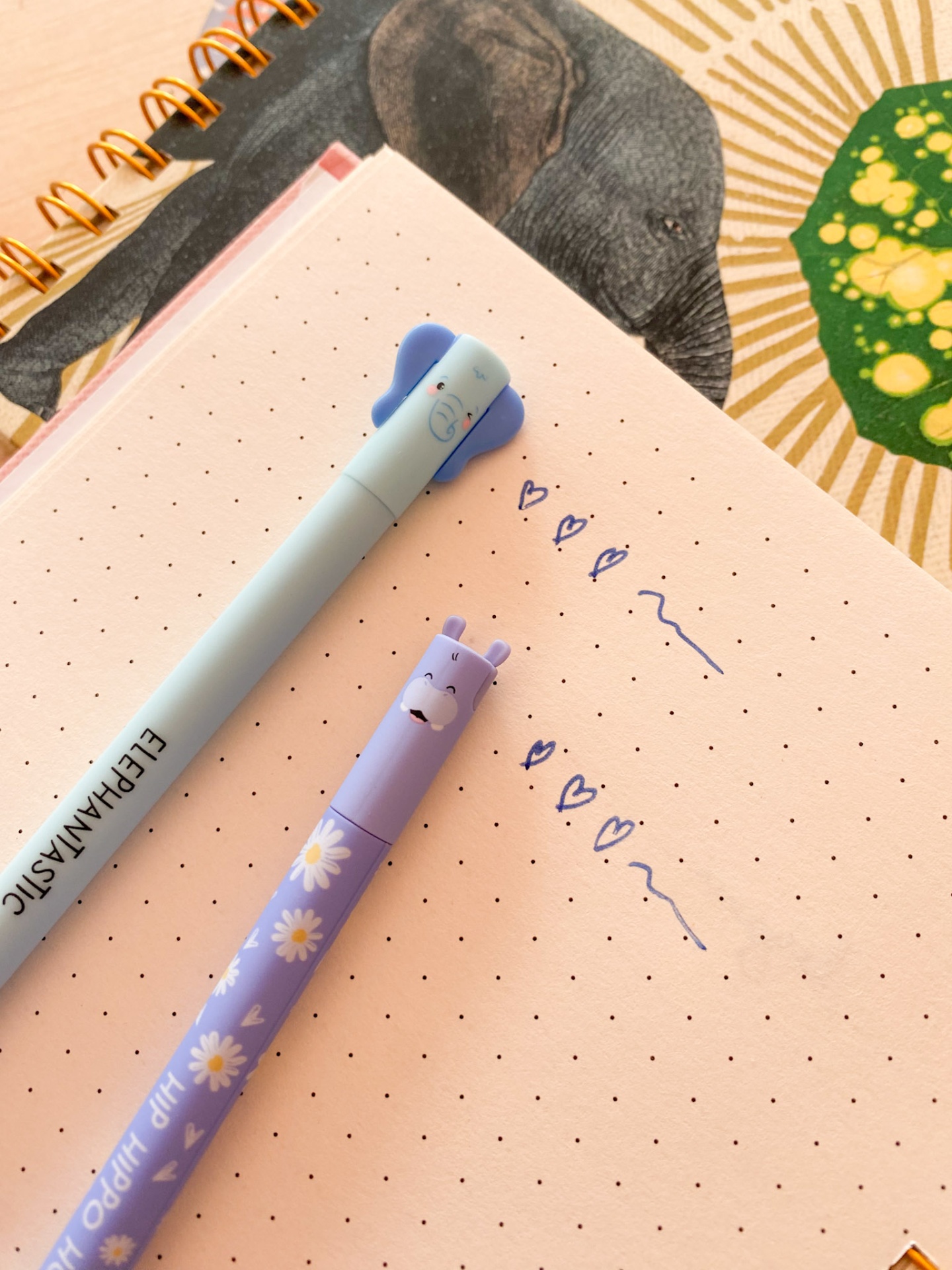Duas canetas sobre caderno pontilhado com desenhos de elefante e flores.