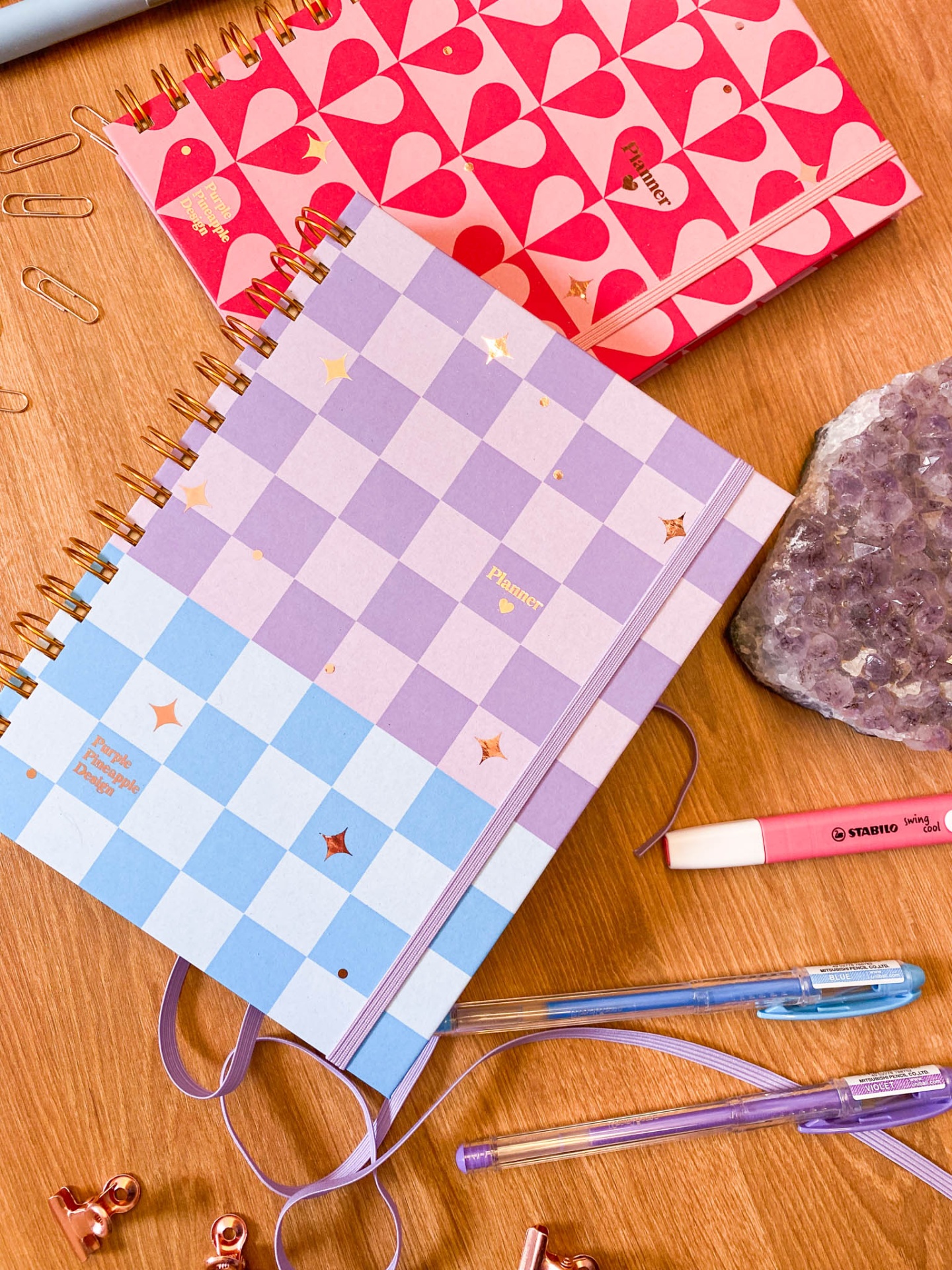Dois cadernos coloridos em padrão geométrico e quadriculado com canetas e pedra ametista sobre mesa de madeira