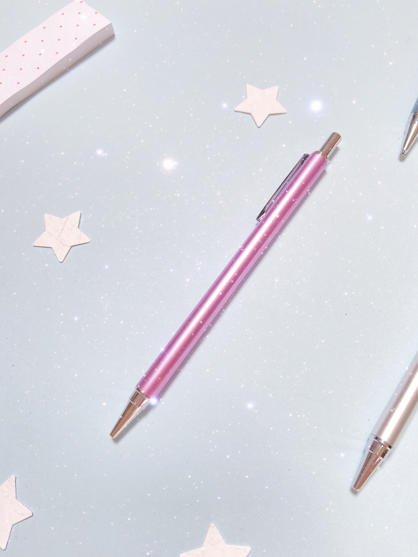 Caneta esferográfica metálica rosa sobre fundo azul com estrelas brancas